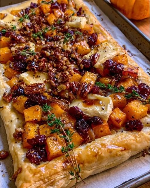 Roasted Butternut Squash & Caramelized Onion Tart with Brie, Cranberries & Maple Pecans There are certain recipes that make the whole kitchen smell like a celebration, and this Roasted Butternut Squash & Caramelized Onion Tart with Brie, Cranberries & Maple Pecans is one of them. I love making this kind of tart when the weather starts getting cooler and I want something that feels a little special without making an entire complicated dinner. The first time I made it, I had roasted butternut squash in the oven, onions slowly turning golden in a skillet, and a sheet of puff pastry waiting on the counter. Then I added Brie. That creamy cheese melting into the warm squash and sweet onions was already wonderful. But once the tart came out of the oven, I scattered over tart dried cranberries and maple-coated pecans, and suddenly it looked like something I'd planned for a holiday table weeks in advance. I hadn't. That's one of the things I love most about this recipe. It looks impressive, but the individual steps are surprisingly simple. You get crisp, buttery pastry, tender caramelized squash, silky onions, creamy Brie, chewy cranberries, and crunchy maple pecans in every bite. It is sweet and savory, creamy and crisp, soft and crunchy—all at once. Why You'll Love This Tart 🍂 Perfect for fall and winter entertaining 🧅 Deeply caramelized onions add incredible savory sweetness 🎃 Roasted butternut squash becomes tender and beautifully caramelized 🧀 Brie melts into the filling for a rich, creamy finish 🍒 Cranberries add little bursts of tart sweetness 🌰 Maple pecans provide an irresistible crunchy topping 🥐 Store-bought puff pastry makes the recipe much easier ✨ Beautiful enough for a holiday table 🥗 Delicious as a vegetarian main course or elegant side dish The combination of squash and caramelized onions is a classic savory-tart pairing, while Brie, cranberries, pecans, and maple bring a festive sweet-savory contrast. Ingredients For the Tart 1 sheet frozen puff pastry, thawed 3 cups peeled and cubed butternut squash, cut into about 1/2-inch cubes 2 large yellow onions, thinly sliced 2 tablespoons olive oil, divided 1 tablespoon butter 1 teaspoon fresh thyme leaves 1/2 teaspoon kosher salt 1/4 teaspoon black pepper 1/2 teaspoon garlic powder 5–6 ounces Brie cheese, cut into small pieces 1 large egg 1 tablespoon water For the Cranberry Topping 1/3 cup dried cranberries 1 tablespoon orange juice 1 teaspoon orange zest 1 tablespoon maple syrup For the Maple Pecans 3/4 cup pecan halves, roughly chopped 1 tablespoon maple syrup 1 tablespoon butter Pinch of salt 1/4 teaspoon cinnamon For Finishing Fresh thyme Flaky sea salt, optional Extra maple syrup, optional How to Make Roasted Butternut Squash & Caramelized Onion Tart 1. Roast the Butternut Squash Start by preheating your oven to 400°F (200°C). Line a large baking sheet with parchment paper. Place the cubed butternut squash on the sheet and toss with: 1 tablespoon olive oil Salt Black pepper Garlic powder Spread the squash into a single layer. Don't crowd the pan too much. Giving the pieces a little room allows the edges to roast instead of simply steaming. Roast for approximately 25–30 minutes, turning once halfway through. You're looking for tender squash with lightly browned, caramelized edges. Roasting the squash first concentrates its flavor and gives the tart much more depth than simply adding raw squash to the pastry. Roasted squash is commonly used in savory tart recipes for exactly this reason. Set the squash aside when finished. 2. Slowly Caramelize the Onions While the squash is roasting, heat the remaining tablespoon of olive oil and the butter in a large skillet over medium-low heat. Add the sliced onions and a small pinch of salt. Cook slowly for about 25–35 minutes, stirring every few minutes. At first, the onions will look like an enormous pile. Don't worry. They shrink dramatically as they cook. Continue cooking until they're soft, deeply golden, and jammy. If the onions begin sticking or browning too quickly, lower the heat and add a tablespoon of water. This is not the place to rush. Slowly cooked onions develop the deep sweet-savory flavor that makes this tart so special. Caramelized onions are also a classic component of squash tarts. Stir in the fresh thyme during the final minute. Remove from the heat. 3. Prepare the Puff Pastry While the filling cools slightly, place the thawed puff pastry on a parchment-lined baking sheet. Gently roll it out just enough to smooth any creases. Using a sharp knife, lightly score a 1/2-inch border around the edge without cutting all the way through. Then prick the center several times with a fork. This helps create a defined, beautifully puffed border while keeping the center from rising too dramatically. Brush the outer border with the beaten egg mixed with water. 4. Layer the Onions Spread the caramelized onions evenly across the center of the pastry. Keep them inside the scored border. The onions should form a thin, even layer rather than one huge mound. 5. Add the Roasted Squash Scatter the roasted butternut squash over the onions. Try to distribute it evenly so every slice gets a little squash. I like leaving some of the golden edges visible because it makes the finished tart look especially pretty. 6. Add the Brie Dot pieces of Brie over the squash. You don't need to remove the rind unless you personally dislike it. Brie rind is edible, and leaving it on helps keep the preparation quick and easy. As the tart bakes, the Brie melts into the squash and onions, creating creamy pockets of cheese throughout. And this is the moment when I usually start getting impatient. Because once the Brie hits the warm squash, you know you're very close to something delicious. 7. Bake the Tart Place the tart in the 400°F oven and bake for approximately 20–25 minutes. The pastry should be: Golden brown Crisp around the edges Puffy along the border The Brie should be melted and soft. If the pastry is browning too quickly before the center is hot, reduce the oven temperature to 375°F for the final few minutes. 8. Make the Cranberry Topping While the tart bakes, place the dried cranberries, orange juice, orange zest, and maple syrup in a small saucepan. Warm over low heat for about 2–3 minutes, just until the cranberries soften slightly and become glossy. Don't boil them. You're simply waking up their flavor and giving them a beautiful little maple-orange coating. Set aside. 9. Make the Maple Pecans Place the chopped pecans in a small skillet over medium-low heat. Add the butter, maple syrup, cinnamon, and salt. Cook for about 3–5 minutes, stirring frequently. The pecans should become fragrant and lightly toasted, with a thin maple coating. Watch them carefully. Pecans can go from perfectly toasted to burnt surprisingly quickly. Transfer them to a plate lined with parchment and let them cool for a few minutes. They'll become crunchier as they cool. 10. Finish the Tart Remove the tart from the oven and let it cool for about 5 minutes. Scatter the maple pecans and cranberries over the top. Finish with fresh thyme and, if you like, a tiny pinch of flaky sea salt. For an extra festive touch, drizzle the tiniest amount of maple syrup over the finished tart. Then slice and serve. The Secret to Perfect Caramelized Onions If there is one part of this recipe worth being patient with, it's the onions. You want them deep golden brown and soft, not merely softened. Keep the heat relatively low and stir occasionally. The natural sugars in the onions gradually caramelize, creating a rich flavor that balances the earthy sweetness of the squash and the creamy Brie. If you rush the process with high heat, the outside can burn before the onions become tender and jammy. So put on some music, make yourself a cup of coffee, and let the onions do their thing. It's worth it. Don't Make the Tart Too Wet This is especially important when working with puff pastry. Your roasted squash should have browned edges rather than being watery. Your caramelized onions should be cooked until most excess moisture has disappeared. And if your Brie is particularly soft, don't pile on too much. The goal is a flaky, crisp pastry base, not a soggy one. A Little Trick for Extra-Crispy Pastry If you have time, place the assembled tart in the refrigerator for 10–15 minutes before baking. Starting with chilled pastry can help the butter in the puff pastry stay firm long enough to create better lift and crispness in the oven. Can I Use Homemade Pastry? Absolutely. A homemade pie crust would give the tart a sturdier, more rustic texture. But for entertaining, I usually reach for store-bought puff pastry. It saves time and gives you that beautiful flaky, golden finish without requiring an afternoon of pastry-making. Puff pastry is also commonly used for squash and Brie tart variations. Easy Variations Add Fresh Sage Replace some of the thyme with fresh sage. Sage and butternut squash are a classic combination. Add Goat Cheese Use a mixture of Brie and goat cheese for a tangier filling. Add Bacon For a non-vegetarian version, sprinkle cooked, crumbled bacon over the tart before adding the cranberries and pecans. Use Walnuts Don't have pecans? Chopped walnuts work beautifully with maple and squash. Add Balsamic A few drops of balsamic glaze over the finished tart add another layer of sweet-tangy flavor. Don't use too much—you want it to complement the Brie rather than overpower everything. Make It More Savory Skip the maple drizzle and increase the herbs. You can also add a pinch of red pepper flakes to the onions. Can I Make This Ahead? Yes, and this is one of the reasons I love this tart for entertaining. The butternut squash can be roasted and the onions caramelized up to 2 days ahead. Keep both refrigerated in separate airtight containers. When you're ready to bake, assemble the tart with the chilled or room-temperature filling. Make the maple pecans shortly before serving for the best crunch. Preparing components ahead of time is a common strategy for squash tarts and makes the final assembly much less stressful. How to Store Leftovers Allow the tart to cool completely. Place leftovers in an airtight container and refrigerate for up to 3 days. For the best texture, reheat slices in a 350°F oven for 8–12 minutes. I don't recommend microwaving if you can avoid it because the pastry will soften. The oven brings the crispness back much better. Can I Freeze This Tart? Yes, although the pastry is best when freshly baked. Let the baked tart cool completely, then wrap individual slices tightly and freeze. For best quality, use within about 1 month. Thaw overnight in the refrigerator and reheat in a 350°F oven until warmed through and crisp. The general idea of freezing and reheating baked puff-pastry tarts is well established, although fresh-baked pastry will always have the crispest texture. What to Serve With This Tart This tart is substantial enough to be a light vegetarian main course, but it also makes a beautiful side dish. Serve it with: Simple arugula salad Mixed green salad with lemon vinaigrette Roasted Brussels sprouts Green beans Cranberry-orange salad Tomato soup Butternut squash soup Herb-roasted chicken Roast turkey Baked salmon For a holiday table, I love serving it alongside a simple green salad. The fresh greens cut through the richness of the Brie and pastry perfectly. Perfect for Thanksgiving and Holiday Gatherings This is one of those recipes that looks right at home on a holiday table. The orange squash, ruby-red cranberries, golden pastry, creamy Brie, and toasted pecans make it naturally festive without requiring elaborate decoration. And unlike some holiday dishes, you don't need to serve it piping hot. It's delicious warm or at room temperature, which makes it much easier to work into a busy dinner spread. Frequently Asked Questions Can I use frozen butternut squash? Yes, although fresh squash generally gives you better roasted edges. If using frozen cubes, roast them directly from frozen and give them enough space on the baking sheet so excess moisture can evaporate. Can I use pre-caramelized onions? Absolutely. If you have leftover caramelized onions from another recipe, this tart is a wonderful way to use them. Do I have to use Brie? No. Camembert, goat cheese, Gruyère, or even sharp white cheddar can work. Brie gives the softest and creamiest result. Can I use fresh cranberries instead of dried? Yes, but fresh cranberries are much more tart and juicy. I'd cook them briefly with maple syrup and orange juice until they soften and become slightly jammy before adding them to the tart. Can I leave out the maple syrup? Yes. The squash and onions already provide natural sweetness. The maple is mainly there to enhance the pecans and bring the flavors together. Why is my puff pastry soggy? The most common reasons are excess moisture from the filling, overcrowding the tart, or not baking it long enough. Make sure your squash is well roasted and your onions are cooked until jammy rather than watery. Can I make mini tarts? Definitely. Cut the puff pastry into smaller rectangles or squares and make individual portions. Reduce the baking time and watch for golden, puffed edges. Is this tart vegetarian? Yes, provided you use vegetarian-friendly Brie and puff pastry. Check packaged ingredients if this is important for your dietary needs. Recipe at a Glance Prep Time: 25 minutes Roasting Time: 25–30 minutes Caramelizing Time: 25–35 minutes Tart Baking Time: 20–25 minutes Total Time: About 1 hour 30 minutes Servings: 6–8 Final Thoughts I think this tart is proof that comfort food doesn't have to be heavy or complicated. You've got sweet roasted butternut squash, golden caramelized onions, creamy Brie, tart cranberries, buttery maple pecans, and flaky pastry—all in one beautiful dish. Every bite has something different going on. Sometimes you get a crispy corner with melted Brie. Sometimes you get a sweet piece of squash with a crunchy pecan. And then you'll get one bite where the cranberry cuts through everything with that little burst of tartness. It's the kind of food I love putting in the middle of the table and letting everyone help themselves. I can imagine serving it on a quiet Sunday afternoon, bringing it to a Thanksgiving gathering, or making it for a cozy dinner when I want something that feels a little more special than the usual weeknight meal. And the best part? It looks like you worked incredibly hard. You don't have to tell anyone how straightforward it really was. Flaky pastry, sweet roasted squash, silky caramelized onions, creamy Brie, tart cranberries, and crunchy maple pecans—this is the kind of fall tart that makes everyone linger around the table for one more slice.