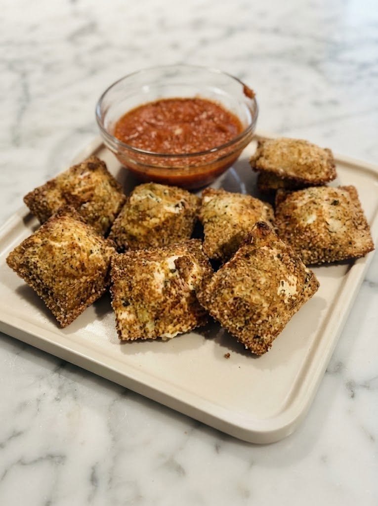 🧀 Keto Toasted Ravioli There are some foods that make you instantly think of a cozy restaurant night, and toasted ravioli is definitely one of them. Crispy on the outside, warm and cheesy in the middle, with a little bowl of marinara sauce waiting for dipping—it’s the kind of appetizer that disappears before anyone even realizes how many they’ve eaten. I wanted that same experience without all the traditional flour and breadcrumbs, so I gave classic toasted ravioli a low-carb makeover. The result? Crispy, golden keto ravioli with a gooey cheese filling and plenty of Italian flavor. I love making these when we’re having a relaxed weekend at home. They feel special enough for a family appetizer spread, but they’re actually pretty simple once you get the ravioli assembled. And if you have a picky eater in the family, this is one of those recipes that usually gets everyone hovering around the kitchen waiting for the first batch. The best part is that you can make them in the air fryer, oven, or skillet, depending on how crispy you want them. ❤️ Why You’ll Love This Recipe Low-carb and keto-friendly compared with traditional toasted ravioli Crispy and golden outside Warm, cheesy filling Perfect for dipping in marinara Easy to customize with different cheeses Great for game day, parties, or weekend snacking Can be cooked in the air fryer or oven Make-ahead friendly Traditional toasted ravioli is generally breaded and fried, while keto ravioli recipes commonly use almond flour or cheese-based alternatives instead of wheat pasta. 🛒 Ingredients For the Keto Ravioli 1 1/2 cups shredded mozzarella cheese 2 oz cream cheese 3/4 cup finely ground almond flour 1 large egg 1/2 tsp xanthan gum 1/2 tsp Italian seasoning 1/4 tsp garlic powder 1/4 tsp salt For the Filling 1/2 cup whole-milk ricotta cheese 1/3 cup shredded mozzarella 2 tbsp grated Parmesan 1/2 tsp Italian seasoning 1/4 tsp garlic powder Pinch of salt Pinch of black pepper For the Crispy Coating 1 large egg 1 tbsp heavy cream 1/2 cup finely grated Parmesan 1/4 cup almond flour 1/2 tsp Italian seasoning 1/4 tsp garlic powder Pinch of salt For Cooking Olive oil spray or a little avocado oil For Serving 1 cup low-carb marinara sauce Extra Parmesan Fresh parsley or basil, optional Red pepper flakes, optional 👩‍🍳 How to Make Keto Toasted Ravioli Step 1: Make the Keto Ravioli Dough Start by preparing the dough. Add the mozzarella and cream cheese to a microwave-safe bowl. Microwave in 20–30 second intervals, stirring between each, until the cheese is melted and smooth. Add the almond flour, xanthan gum, Italian seasoning, garlic powder, salt, and egg. Stir everything together until you have a soft dough. If the dough feels sticky, let it sit for a couple of minutes. It will firm up slightly as it cools. Keto ravioli dough can be more delicate than traditional pasta dough, so don't rush this step. Similar low-carb ravioli recipes use almond flour together with binding ingredients such as xanthan gum and psyllium to create a workable dough. Step 2: Roll Out the Dough Place the dough between two sheets of parchment paper. Roll it out fairly thin—about 1/8 inch thick. Don't make it paper-thin. You want the dough thin enough to resemble ravioli but sturdy enough to hold the filling. Using a round cutter or small glass, cut circles from the dough. Gather the scraps, gently press them together, and roll them out again. You should get approximately 18–20 small ravioli pieces, depending on the size of your cutter. Step 3: Make the Cheese Filling In a small bowl, combine: Ricotta Mozzarella Parmesan Italian seasoning Garlic powder Salt Black pepper Mix until creamy. Place about 1 teaspoon of filling in the center of each dough circle. Don't overfill them. It can be tempting to add a big spoonful of cheese, but too much filling makes the ravioli difficult to seal. Step 4: Seal the Ravioli Fold each dough circle over the filling to create a half-moon shape. Press the edges firmly with your fingers. Then use the tines of a fork to press around the edges. This does two things: it seals the ravioli and gives them that classic homemade look. If an edge doesn't seem to be sticking, lightly moisten it with a tiny amount of water before pressing. Place the finished ravioli on a parchment-lined plate or baking sheet. For easier handling, chill them for about 10–15 minutes before breading. 🥣 Step 5: Prepare the Keto Coating In one shallow bowl, whisk together the egg and heavy cream. In another bowl, combine: Parmesan Almond flour Italian seasoning Garlic powder Salt Dip each ravioli into the egg mixture, allowing the excess to drip off. Then gently press it into the Parmesan-almond flour coating. Make sure both sides are covered. This is where the magic starts happening. That simple combination of Parmesan and almond flour creates a wonderfully savory coating without traditional breadcrumbs. 🔥 Step 6: Cook the Ravioli Air Fryer Method Preheat your air fryer to 375°F (190°C). Lightly spray the basket with oil. Arrange the ravioli in a single layer, leaving a little room between each piece. Lightly spray the tops with oil. Air fry for approximately 7–10 minutes, flipping halfway through, until golden and crisp. Keep a close eye on them toward the end because Parmesan can brown quickly. Oven Method Preheat your oven to 425°F (220°C). Place the coated ravioli on a parchment-lined baking sheet. Lightly spray with olive or avocado oil. Bake for 10–14 minutes, flipping halfway through. They're ready when the coating is golden and crisp. Skillet Method Heat a thin layer of avocado or olive oil in a skillet over medium heat. Cook the ravioli for approximately 2–3 minutes per side, carefully turning once the first side is golden. Transfer to a paper towel-lined plate for a minute before serving. Traditional toasted ravioli is commonly fried until golden, while oven and air-fryer approaches provide an easier way to achieve a crisp exterior with less oil. 🍅 The Best Marinara for Dipping Don't skip the marinara. Warm about 1 cup of low-carb marinara sauce in a small saucepan over low heat. For extra flavor, stir in: A pinch of Italian seasoning A little garlic powder Red pepper flakes A spoonful of Parmesan Serve the warm marinara in a little bowl right in the center of the platter. Then arrange the toasted ravioli around it. It's almost impossible to resist. ✨ Tips for Perfect Keto Toasted Ravioli Don't overfill them A teaspoon of filling is plenty. Too much cheese can burst through the dough while cooking. Keep the dough warm but manageable If your dough becomes stiff while you're working, warm it very gently. If it becomes too sticky, let it cool for a minute. Seal the edges well Press firmly with your fingers before using the fork. A good seal keeps the filling inside where it belongs. Don't overcrowd the air fryer Cook in batches if necessary. Air needs to circulate around each ravioli for the best crispness. Use finely grated Parmesan Very coarse Parmesan doesn't cling to the ravioli as evenly. Fine Parmesan gives you a more uniform crust. Watch the cooking time Keto coatings can brown faster than traditional breadcrumbs, particularly because of the Parmesan. 🌶️ Easy Variations Pepperoni Pizza Ravioli Add finely chopped pepperoni and mozzarella to the filling. Serve with warm marinara. Spinach & Ricotta Ravioli Sauté a handful of chopped spinach, squeeze out excess moisture, and mix it into the ricotta filling. Garlic Parmesan Ravioli Add extra garlic powder and Parmesan to the coating. Finish with melted garlic butter and parsley. Spicy Ravioli Add crushed red pepper flakes to the filling and coating. Serve with spicy marinara. Meat Ravioli Mix a small amount of cooked, finely crumbled Italian sausage or ground beef into the cheese filling. Make sure the meat is completely cooked and cooled before adding it. 🥗 What to Serve With Keto Toasted Ravioli These make a fantastic appetizer, but you can easily turn them into part of a larger meal. Try serving them with: Italian chopped salad Caesar salad Garlic butter zucchini Roasted broccoli Sautéed spinach Zucchini noodles with marinara Grilled chicken Meatballs Extra marinara and Parmesan For a party, put the ravioli on a large platter with marinara, ranch, garlic butter, and spicy tomato sauce for dipping. 🧊 Can You Make Keto Toasted Ravioli Ahead? Absolutely. Prepare and seal the ravioli, then place them on a parchment-lined tray in a single layer. Freeze until firm. Once frozen, transfer them to an airtight freezer container or freezer bag. When you're ready to cook them, you can generally cook them from chilled or frozen, adding a few extra minutes to the cooking time. Watch them closely during the first batch because appliances vary. Freezing keto ravioli before cooking is also used in other low-carb ravioli methods because it helps the delicate dough maintain its shape. 🧺 How to Store Leftovers Store cooked ravioli in an airtight container in the refrigerator for up to 3 days. For the best texture, reheat them in: Air fryer: 350°F for 3–5 minutes Oven: 375°F for 5–8 minutes I don't recommend microwaving them if crispiness matters. They'll still taste good, but the coating will soften. ❓ Frequently Asked Questions Is toasted ravioli keto? Traditional toasted ravioli usually isn't keto because both the pasta and breadcrumb coating contain wheat-based carbohydrates. A keto version needs low-carb ravioli dough and a flour-free or low-carb coating. Can I use store-bought keto ravioli? Yes. If you can find a low-carb ravioli product that you enjoy, you can skip the homemade dough and simply bread and cook the ravioli according to this method. Can I make these without almond flour? You can experiment with finely crushed pork rinds or another keto-friendly crumb alternative for the coating. For the ravioli dough itself, you'll need a different low-carb dough recipe rather than simply replacing almond flour one-for-one. Can I fry them? Yes. Heat a shallow layer of oil over medium heat and cook until golden on both sides, about 2–3 minutes per side. Work in batches so the temperature doesn't drop too much. Why did my ravioli open? Usually this happens because the edges weren't sealed firmly enough or there was too much filling. Press around the filling first, then firmly seal and crimp the edges. Can I use mozzarella instead of ricotta? Absolutely. You can make the filling with mozzarella, Parmesan, and cream cheese for an especially gooey center. What sauce goes best with toasted ravioli? A simple low-carb marinara is my favorite. Alfredo, garlic butter, pesto, or a creamy tomato sauce are also delicious. 📝 Recipe at a Glance Prep Time: 30 minutes Chill Time: 10–15 minutes Cook Time: 10–15 minutes Total Time: About 55–60 minutes Servings: 4 Course: Appetizer / Snack Cuisine: Italian-inspired Cooking Methods: Air fryer, oven, or skillet 🧀 Keto Toasted Ravioli Recipe Ingredients Ravioli dough 1 1/2 cups mozzarella 2 oz cream cheese 3/4 cup almond flour 1 egg 1/2 tsp xanthan gum 1/2 tsp Italian seasoning 1/4 tsp garlic powder 1/4 tsp salt Filling 1/2 cup ricotta 1/3 cup mozzarella 2 tbsp Parmesan 1/2 tsp Italian seasoning 1/4 tsp garlic powder Salt and pepper Coating 1 egg 1 tbsp heavy cream 1/2 cup Parmesan 1/4 cup almond flour 1/2 tsp Italian seasoning 1/4 tsp garlic powder Pinch of salt For serving Low-carb marinara Parmesan Fresh basil or parsley Instructions Melt mozzarella and cream cheese together until smooth. Mix in almond flour, xanthan gum, egg, and seasonings to form a dough. Roll the dough between parchment sheets to about 1/8 inch thick. Cut into small circles. Combine the filling ingredients. Place about 1 teaspoon filling onto each dough circle. Fold, seal, and crimp the edges with a fork. Chill for 10–15 minutes. Whisk egg and heavy cream together. Mix Parmesan, almond flour, and seasonings separately. Dip ravioli in egg mixture, then coat with the Parmesan mixture. Air fry at 375°F for 7–10 minutes, bake at 425°F for 10–14 minutes, or pan-fry for 2–3 minutes per side. Serve immediately with warm low-carb marinara. ❤️ Final Thoughts This is one of those recipes that makes keto eating feel anything but boring. You still get that satisfying crunch, the warm cheesy center, the Italian seasoning, and that little bowl of marinara begging to be dipped into. When these come out of the air fryer golden and bubbling, everyone tends to gather around the kitchen—and honestly, that's my favorite kind of recipe. Make a batch for a weekend movie night, serve them at your next gathering, or keep a few in the freezer for those evenings when you want something comforting without making an entire dinner. Crispy, cheesy, dunkable, and keto-friendly—these toasted ravioli are definitely worth making. 🧀🍅
