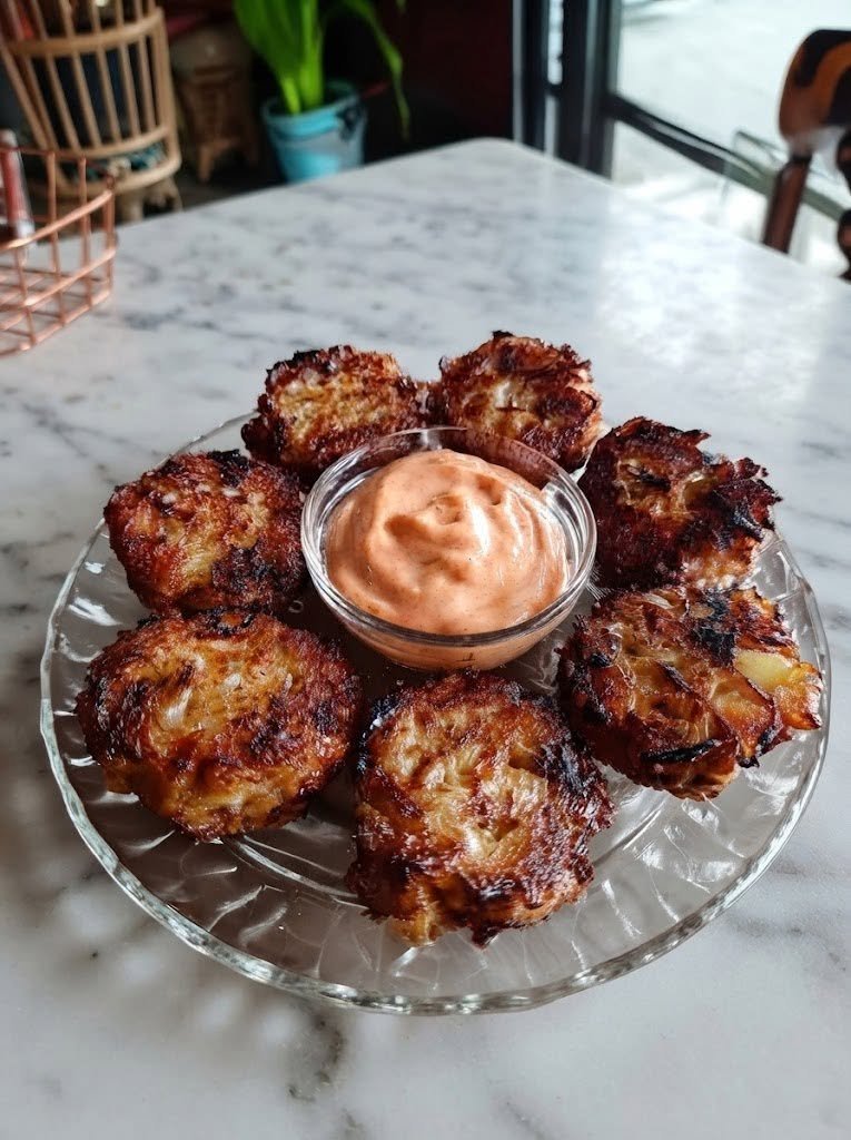 Keto Crispy Cheese & Onion Fritters with Spicy Mayo There are days when I don't want a complicated meal—I just want something crispy, cheesy, savory, and completely satisfying. That's exactly where these Keto Crispy Cheese & Onion Fritters with Spicy Mayo come in. I love recipes like this because they feel like a little treat. The outside gets beautifully golden and crisp while the inside stays soft, cheesy, and full of sweet onion flavor. Then you dip that warm fritter into cool, creamy spicy mayo and suddenly a simple handful of ingredients tastes like something you'd order as an appetizer at your favorite restaurant. I first started making these when I was craving something crunchy but wanted to keep things low-carb. They quickly became one of those recipes that everyone seems to hover around while they're cooking. The hardest part? Getting enough onto the serving plate before somebody eats them straight from the skillet. Why You'll Love These Keto Fritters 🧀 Crispy, golden, and wonderfully cheesy 🧅 Packed with savory-sweet onion flavor 🌶️ Served with creamy spicy mayo 🥚 Easy to make with simple ingredients 🍳 Cooked in a skillet rather than deep-fried 🥑 Naturally low-carb and keto-friendly 👨‍👩‍👧 Great as an appetizer, snack, or side dish ⏱️ Ready in about 30 minutes Ingredients For the Cheese & Onion Fritters 2 cups shredded mozzarella cheese 1/2 cup finely shredded cheddar cheese 1/2 medium yellow onion, very finely diced 2 large eggs 1/3 cup finely ground almond flour 2 tablespoons grated Parmesan cheese 1/2 teaspoon garlic powder 1/2 teaspoon smoked paprika 1/4 teaspoon black pepper 1/4 teaspoon salt 2 tablespoons chopped fresh parsley 2–3 tablespoons olive oil or avocado oil, for frying For the Spicy Mayo 1/2 cup mayonnaise 1–2 tablespoons hot sauce 1/2 teaspoon smoked paprika 1/4 teaspoon garlic powder 1 teaspoon fresh lemon juice Pinch of salt How to Make Keto Crispy Cheese & Onion Fritters 1. Prepare the Onion Finely dice the onion. This matters more than you might think. Large pieces of onion can make the fritters difficult to hold together, while very finely chopped onion distributes beautifully throughout the mixture. If your onion seems particularly wet, pat it gently with a paper towel before adding it to the batter. 2. Make the Fritter Mixture Add the mozzarella, cheddar, onion, eggs, almond flour, Parmesan, garlic powder, smoked paprika, black pepper, salt, and parsley to a large bowl. Mix everything thoroughly. At first, the mixture may look more like a chunky cheese mixture than traditional fritter batter. That's exactly what you want. The eggs and almond flour help bind everything together while the cheese melts during cooking. 3. Let the Mixture Rest Let the mixture sit for about 5 minutes. This gives the almond flour a chance to absorb some moisture. If the mixture still seems too loose to shape, add another tablespoon of almond flour. Don't add too much, though. The goal is a cheesy fritter, not a dense almond-flour pancake. 4. Shape the Fritters Scoop out approximately 2 tablespoons of the mixture for each fritter. Gently shape into a small patty. Keep them relatively thin—about 1/2 inch thick. Thin fritters cook more evenly and develop those wonderfully crispy edges. Don't worry if they're not perfectly round. A little rustic character makes them look homemade. 5. Heat the Skillet Heat a large nonstick or well-seasoned skillet over medium heat. Add enough olive oil or avocado oil to lightly coat the bottom. You want the oil hot enough that the fritters begin sizzling as soon as they hit the pan. But don't make it screaming hot. If the pan is too hot, the cheese can brown before the center has had time to set. 6. Cook the Fritters Carefully place the fritters into the skillet, leaving a little space between each one. Cook for approximately 3–4 minutes on the first side. Don't move them around. This is important. Let the bottom develop a golden crust before attempting to flip them. Once the edges look set and the underside is deeply golden, carefully flip each fritter. Cook for another 2–3 minutes on the other side. You should end up with crisp, browned edges and melted cheese throughout. 7. Drain Transfer the cooked fritters to a plate lined with paper towels or a wire rack. Sprinkle with a tiny pinch of salt while they're still hot. Then try not to eat one immediately. Although I won't blame you if you do. How to Make the Spicy Mayo While the fritters cook, make the dipping sauce. Add the mayonnaise, hot sauce, smoked paprika, garlic powder, lemon juice, and salt to a small bowl. Stir until completely smooth. Taste it. Want more heat? Add another splash of hot sauce. Want it milder? Add a little more mayonnaise. For an extra smoky version, add another pinch of smoked paprika. The Secret to Extra-Crispy Fritters There are a few little tricks that make a huge difference. Don't make them too thick A thinner fritter gives you more crispy surface area and allows the center to cook before the outside becomes too dark. Don't overcrowd the pan Give each fritter some room. If you crowd the skillet, the temperature drops and the fritters can steam rather than crisp. Use enough oil You don't need to deep-fry them, but the pan should have enough oil to encourage even browning. Let them cook undisturbed Once they're in the pan, resist the urge to move them. The cheese needs time to form a crust. Use a nonstick skillet Because these fritters contain melted cheese, a good nonstick skillet makes flipping considerably easier. What Kind of Cheese Works Best? Mozzarella is excellent because it melts beautifully and gives the fritters that stretchy, cheesy texture. Cheddar adds stronger flavor and helps with browning. Parmesan brings a salty, nutty flavor and contributes to the crispy edges. You can change the cheese combination depending on what you have. Try These Combinations Mozzarella + cheddar Cheddar + Monterey Jack Mozzarella + Parmesan Gouda + cheddar Pepper Jack + mozzarella Pepper Jack is especially good if you're making the spicy version. Can I Use Coconut Flour? Yes, but don't substitute it cup-for-cup for almond flour. Coconut flour absorbs much more moisture, so you'll need considerably less. For the most predictable result, I recommend sticking with finely ground almond flour. Make Them Spicier If you like heat, there are plenty of ways to turn these up. Add: 1/4 teaspoon cayenne pepper Finely diced jalapeño Red pepper flakes Pepper Jack cheese Extra hot sauce A pinch of chipotle powder My favorite combination is Pepper Jack cheese with a little smoked paprika and a spicy mayo on the side. Make Them Milder For a family-friendly version, skip the cayenne and use mild cheddar. You can also reduce the hot sauce in the mayo to just a teaspoon or two. The fritters themselves aren't particularly spicy, so the dipping sauce is easy to customize. Add Bacon Crispy bacon and cheese are almost impossible to argue with. Cook 3–4 slices of bacon until crisp, crumble them finely, and fold them into the fritter mixture. Because bacon adds salt, taste the mixture before adding the full amount of salt. Add Fresh Herbs Fresh herbs make these taste brighter. Try: Chives Parsley Dill Green onion Cilantro Chives are especially delicious with the cheese and onion combination. What to Serve With Cheese & Onion Fritters These fritters can play several different roles. As an Appetizer Pile them onto a platter with spicy mayo in the center. Add some sliced vegetables or pickles for a simple snack board. With Breakfast Serve them alongside: Fried eggs Scrambled eggs Avocado Bacon Sausage They're an excellent alternative to hash browns. With Dinner Serve them as a side dish with: Grilled chicken Steak Burgers Roast beef Salmon Grilled vegetables As a Snack Honestly, you don't need an excuse. Warm fritters and spicy mayo make a pretty excellent afternoon snack. A Fresh Topping Makes Them Even Better Because the fritters are rich and cheesy, I love adding something fresh on top. Try: Chopped parsley Sliced green onions Fresh cilantro Pickled jalapeños A squeeze of lemon Diced avocado That little touch of freshness balances the richness beautifully. Can I Make These Ahead? Yes, but they're at their crispiest when freshly cooked. You can prepare the fritter mixture several hours ahead and keep it covered in the refrigerator. When you're ready to cook, shape the patties and fry them fresh. This is especially convenient when you're preparing food for guests. How to Store Leftovers Allow the fritters to cool before transferring them to an airtight container. Refrigerate for up to 3–4 days. Keep the spicy mayo in a separate covered container. For the best texture, reheat the fritters in a skillet, oven, toaster oven, or air fryer rather than the microwave. How to Reheat Them Air Fryer Heat at 350°F (175°C) for about 3–5 minutes. Oven Place them on a baking sheet and heat at 375°F (190°C) for about 8–10 minutes. Skillet Warm over medium-low heat for a few minutes per side. The goal is to warm them without burning the cheese. Can You Freeze Cheese Fritters? Yes. Allow the cooked fritters to cool completely. Place them on a baking sheet in a single layer and freeze until firm. Then transfer them to a freezer-safe bag or container. Freeze for up to about 2 months for the best quality. Reheat from frozen in an air fryer or oven until hot and crisp. I recommend making the spicy mayo fresh rather than freezing it. Troubleshooting My fritters are falling apart. The mixture may need a little more binder. Try adding another tablespoon of almond flour and let the mixture sit for a few minutes. Also make sure the patties aren't too thick. My fritters are sticking to the pan. Make sure your skillet is properly heated and lightly coated with oil. A good nonstick skillet makes this much easier. Also, don't try to flip them too early. My fritters aren't crispy. The pan may not have been hot enough, or the fritters may have been too thick. Flatten them slightly and make sure you hear a gentle sizzle when they hit the skillet. My fritters are burning before they're cooked. Lower the heat to medium-low. Cheese browns quickly, so moderate heat is usually better than high heat. The mixture is too wet. Add another tablespoon of almond flour and let it rest for 5 minutes. Avoid adding lots of flour at once. Frequently Asked Questions Are these keto-friendly? Yes, they're designed to be low-carb and keto-friendly, using cheese and almond flour rather than wheat flour. Exact carbohydrate amounts will vary depending on the brands of cheese, mayonnaise, almond flour, and hot sauce you use. Can I make these without almond flour? You can experiment with another low-carb binder, such as a small amount of coconut flour, but the amount will need to be adjusted because coconut flour absorbs much more liquid. Can I use pre-shredded cheese? Yes, although freshly shredded cheese often melts more smoothly. If using pre-shredded cheese, check the ingredient label if you're tracking carbohydrates closely. Can I make them in the oven? Yes. Place the shaped fritters on a parchment-lined baking sheet and bake at 400°F (200°C) until golden, flipping once halfway through. They won't have quite the same skillet-fried crust, but they're still delicious. Can I air-fry them? Yes. Air fry at approximately 375°F (190°C) until golden and crisp, turning halfway through. Keep an eye on the first batch because air fryers vary. What can I use instead of mayonnaise? For the dipping sauce, you can use sour cream or a mixture of sour cream and mayonnaise. Can I make the spicy mayo ahead? Absolutely. Keep it refrigerated in a covered container for up to several days and stir before serving. What onion should I use? Yellow onion is my favorite, but white or sweet onion works beautifully too. Green onions are another excellent option when you want a milder onion flavor. Recipe at a Glance Prep Time: 10 minutes Cook Time: 15–20 minutes Total Time: About 30 minutes Servings: 4 Yield: About 10–12 fritters Final Thoughts These Keto Crispy Cheese & Onion Fritters with Spicy Mayo are exactly the sort of recipe that reminds me why simple ingredients can be so much fun. You don't need a long ingredient list. You don't need fancy equipment. You just need good cheese, a little onion, a few seasonings, and a hot skillet. The outside gets beautifully crisp while the inside stays warm and cheesy. Then you dunk that golden fritter into the spicy mayo and get the perfect combination of crunchy, creamy, savory, and slightly spicy. I love serving these when family is around because they disappear almost ridiculously quickly. They're also perfect for those evenings when I'm craving something indulgent but still want to keep the meal low-carb. Make a batch, put the spicy mayo in the middle of the table, and watch everyone reach for one. Then another. And probably another. Crispy edges, gooey cheese, sweet onion, and a creamy spicy dip—these little keto fritters are seriously hard to resist.