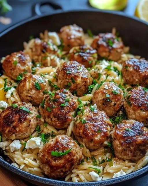 Lemon Chicken Feta Meatballs with Garlic Orzo Some dinners just feel like they belong on repeat. This Lemon Chicken Feta Meatballs with Garlic Orzo recipe is one of those meals for me. It's bright, comforting, fresh, and incredibly satisfying without feeling overly heavy. I made these meatballs for a family dinner recently, and I honestly wasn't sure how everyone would react to chicken meatballs. Sometimes people hear "chicken meatballs" and immediately assume they're going to be dry. These were anything but. The meatballs are tender and juicy, packed with garlic, lemon, herbs, and salty feta. Then they're served over buttery garlic orzo that soaks up all those wonderful Mediterranean flavors. I added a little fresh parsley and lemon at the end, and the whole kitchen smelled amazing. Everyone loved it. One person went back for more meatballs. Another kept spooning extra orzo onto their plate. And I found myself scraping the bottom of the pan for those little golden bits left behind from cooking the meatballs. That's when you know dinner is a keeper. What I love most is that this recipe feels special enough for a weekend dinner but is still straightforward enough for a busy weeknight. It's one skillet-style meal that brings together tender chicken, creamy feta, lemon, garlic, herbs, and comforting orzo. And honestly, I don't think you can go wrong with that combination. ❤️ Why You'll Love These Lemon Chicken Feta Meatballs Tender and juicy chicken meatballs Bright lemon and garlic flavor Salty, creamy feta throughout Fresh Mediterranean herbs Buttery garlic orzo Easy enough for a weeknight Great for family dinners Beautiful enough for entertaining Makes wonderful leftovers Everything feels fresh but still comforting The combination of lemon and feta is especially good here. The lemon keeps the dish bright while the feta adds richness and saltiness. 🛒 Ingredients For the Chicken Feta Meatballs 1 pound ground chicken ½ cup crumbled feta cheese ½ cup breadcrumbs 1 large egg 3 cloves garlic, finely minced 1 teaspoon lemon zest 1 tablespoon fresh lemon juice 2 tablespoons chopped fresh parsley 1 tablespoon chopped fresh dill ½ teaspoon dried oregano ½ teaspoon salt ½ teaspoon freshly ground black pepper 1 tablespoon olive oil, for cooking For the Garlic Orzo 1 cup uncooked orzo 2 tablespoons olive oil 3 cloves garlic, minced 2½ cups chicken broth ½ teaspoon dried oregano ¼ teaspoon black pepper ½ cup crumbled feta 1 tablespoon butter 1 tablespoon fresh lemon juice 1 teaspoon lemon zest 2 tablespoons chopped fresh parsley Optional Garnishes Extra feta Fresh dill Lemon wedges Fresh parsley Cucumber slices Kalamata olives Red pepper flakes 🍋 A Little Lemon Makes a Big Difference The lemon isn't just there for decoration. It helps balance the richness of the chicken, feta, and orzo. I like using both lemon zest and fresh lemon juice. The zest gives you that fragrant citrus aroma, while the juice provides acidity. If you love lemon, serve extra wedges alongside the finished dish. 👩‍🍳 How to Make Lemon Chicken Feta Meatballs with Garlic Orzo 1. Prepare the Meatball Mixture Add the ground chicken to a large mixing bowl. Add: Feta Breadcrumbs Egg Garlic Lemon zest Lemon juice Parsley Dill Oregano Salt Black pepper Mix gently with your hands or a fork until everything is just combined. Try not to overmix. Overworking ground chicken can make the meatballs dense. 🧆 2. Shape the Meatballs Using your hands or a small cookie scoop, form the mixture into meatballs. Aim for approximately 1½ inches each. You should get around 16–20 meatballs, depending on their size. Don't worry if they're not perfectly identical. Homemade meatballs are allowed to have personality. 🔥 3. Brown the Meatballs Heat olive oil in a large skillet over medium heat. Once hot, carefully add the meatballs. Cook for approximately 8–10 minutes, turning them occasionally so they brown on multiple sides. You don't need to cook them completely through at this stage. You're primarily looking for a beautiful golden-brown exterior. Transfer the meatballs to a clean plate. 🧄 4. Start the Garlic Orzo Don't clean the skillet. Those browned bits left behind are flavor. Add the olive oil and minced garlic. Cook for about 30 seconds, just until fragrant. Add the uncooked orzo. Stir for about a minute, allowing the orzo to lightly toast. This tiny step gives it an extra layer of flavor. 🥣 5. Add the Broth Pour the chicken broth into the skillet. Add oregano and black pepper. Stir everything together. Bring the mixture to a gentle simmer. 🍲 6. Cook the Orzo Reduce the heat to medium-low. Cook for approximately 8–10 minutes, stirring frequently. Orzo can stick to the bottom of the pan, so don't walk away completely. Add a small splash of broth or water if the pan becomes too dry before the orzo is tender. You want the finished orzo to be creamy and tender but not mushy. 🧆 7. Return the Meatballs Once the orzo is nearly cooked, nestle the browned meatballs back into the skillet. Cover loosely and cook for another 5–7 minutes, or until the meatballs are completely cooked through. Chicken should reach an internal temperature of 165°F (74°C). The meatballs will finish cooking while their juices mingle with the garlic orzo. 🧈 8. Finish the Orzo Turn off the heat. Add: Butter Lemon juice Lemon zest Feta Fresh parsley Stir gently. The feta will soften slightly and become wonderfully creamy while still retaining some little salty pieces throughout the orzo. Taste and adjust the seasoning. 🌿 9. Garnish and Serve Scatter more parsley and dill over the top. Add extra crumbled feta. Place lemon wedges around the skillet. If you like heat, sprinkle with red pepper flakes. Then bring the entire skillet straight to the table. That's my favorite way to serve it. ⭐ Tips for Tender Chicken Meatballs Don't overmix Mix the ingredients only until combined. Don't make them too large Smaller meatballs cook more evenly and brown beautifully. Don't overcrowd the pan If your skillet is small, brown the meatballs in batches. Don't skip the feta It adds moisture, saltiness, and flavor. Use fresh lemon Fresh lemon juice makes a noticeable difference. Use a thermometer Chicken meatballs should reach 165°F (74°C) internally. 🧄 Make the Orzo Extra Creamy If you prefer a creamier orzo, add one of these at the end: 2 tablespoons heavy cream 2 tablespoons Greek yogurt 2 ounces cream cheese Extra feta If using Greek yogurt, stir it in after removing the skillet from the heat to prevent curdling. 🌶️ Make It Spicy This recipe is wonderful with a little heat. Add: Red pepper flakes Crushed chili Aleppo pepper Pinch of cayenne You can also drizzle the finished dish with a little chili oil. 🥒 Add More Vegetables You can easily turn this into a vegetable-packed dinner. Try adding: Spinach Stir a few handfuls into the orzo during the final minutes. Cherry Tomatoes Add them during the last few minutes so they soften and release their juices. Zucchini Sauté diced zucchini before adding the orzo. Roasted Red Peppers Slice and stir them into the finished dish. Artichoke Hearts Drain and chop before folding them into the orzo. 🫒 Mediterranean-Style Additions For even more Mediterranean flavor, add: Kalamata olives Artichoke hearts Roasted red peppers Cucumber Cherry tomatoes Fresh dill Fresh oregano Extra feta The more colorful the skillet, the more inviting it becomes. 🍋 Make a Creamy Lemon Sauce If you want extra sauce, mix: ½ cup Greek yogurt 1 tablespoon lemon juice 1 teaspoon lemon zest 1 small grated garlic clove Pinch of salt 1–2 tablespoons water Drizzle it over the meatballs just before serving. It's fresh, creamy, and delicious with the garlic orzo. 🥗 What to Serve With Chicken Feta Meatballs This meal is already quite complete, but you can serve it with: Greek salad Cucumber tomato salad Roasted vegetables Grilled zucchini Steamed broccoli Hummus Tzatziki Warm pita Olives A simple Greek salad is probably my favorite side. The crisp vegetables and tangy dressing balance the warm, comforting orzo perfectly. 🍷 Dinner Party Version If you're serving this to guests, keep everything in the skillet and garnish generously. Add: Fresh parsley Dill Lemon wedges Extra feta Kalamata olives Serve with warm crusty bread and a big salad. It looks beautiful straight from the skillet, and there's something wonderfully relaxed about putting a big pan in the middle of the table and letting everyone serve themselves. 🧆 Can I Bake the Meatballs Instead? Yes. Place the shaped meatballs on a parchment-lined baking sheet. Bake at 400°F (200°C) for approximately 18–22 minutes, depending on their size. Check that the center reaches 165°F (74°C). You can then prepare the garlic orzo separately and serve the baked meatballs over it. 🔥 Can I Air Fry the Meatballs? Yes. Preheat the air fryer to approximately 400°F (200°C). Arrange the meatballs in a single layer. Cook for about 10–14 minutes, turning halfway through. Because air fryers vary, check the internal temperature rather than relying solely on the cooking time. 🧀 Can I Use Another Cheese? Feta is my first choice because it gives the dish its distinctive Mediterranean flavor. But you can experiment with: Goat cheese Parmesan Ricotta Cotija The flavor and texture will change, but the recipe can still work. 🥛 Can I Make This Gluten-Free? Yes. Use gluten-free breadcrumbs in the meatballs and a gluten-free pasta alternative in place of traditional orzo. Always check ingredient labels if you're avoiding gluten strictly. 🧊 How to Store Leftovers Allow the dish to cool before transferring it to airtight containers. Refrigerate for up to 3–4 days. Store any fresh garnishes separately when possible. 🔥 How to Reheat The orzo thickens as it sits. When reheating, add a splash of chicken broth or water. Warm gently in a skillet over medium-low heat, stirring occasionally. You can also microwave individual portions, adding a little broth before heating. ❄️ Can You Freeze This Recipe? The meatballs freeze very well. The cooked orzo can also be frozen, although its texture may become slightly softer after thawing. For the best result, freeze the meatballs separately and make fresh orzo when possible. If freezing the complete dish, cool it completely, portion it into freezer-safe containers, and use within a few months for best quality. ❓ Frequently Asked Questions How do I keep chicken meatballs from becoming dry? Don't overmix the meat mixture, don't overcook the meatballs, and use a thermometer to remove them once they reach 165°F (74°C). Can I use ground turkey instead? Yes. Ground turkey works very well as a substitute for ground chicken. Can I use frozen spinach? Yes, if you'd like to add spinach. Thaw it and squeeze out excess moisture before adding it to the recipe. Can I make the meatballs ahead? Absolutely. Shape the meatballs up to a day ahead and refrigerate them covered until you're ready to cook. Can I make the meatballs without breadcrumbs? Yes. You can substitute another binder such as almond flour or crushed pork rinds, although the texture will change. Can I use whole-wheat orzo? Yes. Just check the package cooking time because whole-wheat orzo may require a little longer to cook. Why is my orzo sticky? Orzo releases starch as it cooks, which naturally makes the dish creamy. Stir regularly and add broth as needed. Can I use water instead of chicken broth? Yes, but broth gives the orzo much more flavor. Can I add cream? Absolutely. A splash of cream at the end creates a richer, creamier version. Can I make this dairy-free? Yes, but you'll need to replace the feta and butter with dairy-free alternatives. How much lemon should I use? Start with the amount in the recipe and add more at the end according to your taste. What herbs work best? Parsley and dill are my favorites. Fresh oregano, mint, or basil can also work. 📝 Recipe at a Glance Recipe: Lemon Chicken Feta Meatballs with Garlic Orzo Prep Time: 20 minutes Cook Time: 30 minutes Total Time: About 50 minutes Servings: 4–5 Category: Dinner Cuisine: Mediterranean-inspired Method: Stovetop Ingredients Chicken Meatballs 1 pound ground chicken ½ cup crumbled feta ½ cup breadcrumbs 1 egg 3 cloves garlic 1 teaspoon lemon zest 1 tablespoon lemon juice 2 tablespoons parsley 1 tablespoon dill ½ teaspoon oregano ½ teaspoon salt ½ teaspoon black pepper 1 tablespoon olive oil Garlic Orzo 1 cup uncooked orzo 2 tablespoons olive oil 3 cloves garlic 2½ cups chicken broth ½ teaspoon oregano ¼ teaspoon black pepper ½ cup feta 1 tablespoon butter 1 tablespoon lemon juice 1 teaspoon lemon zest 2 tablespoons parsley Instructions Combine ground chicken, feta, breadcrumbs, egg, garlic, lemon, herbs, salt, and pepper. Mix gently until just combined. Shape into 16–20 meatballs. Heat olive oil in a large skillet. Brown meatballs for approximately 8–10 minutes, turning regularly. Remove meatballs and set aside. Add garlic and olive oil to the skillet. Add orzo and toast briefly. Pour in chicken broth. Add oregano and pepper. Simmer for 8–10 minutes, stirring regularly. Return meatballs to the skillet. Cover loosely and cook another 5–7 minutes. Check that chicken reaches 165°F (74°C). Remove from heat. Stir in butter, lemon juice, lemon zest, feta, and parsley. Garnish with fresh herbs and extra feta. Serve with lemon wedges. ❤️ The Kind of Dinner Everyone Remembers I think some recipes become favorites because they are complicated and impressive. Others become favorites because they simply make everyone happy. This is definitely the second kind. The first time I made these lemon chicken feta meatballs, I wasn't trying to create anything fancy. I just wanted a comforting dinner that had plenty of flavor. But when those golden meatballs were sitting over creamy garlic orzo, covered with feta, fresh herbs, and little bursts of lemon, it felt like so much more. It felt like the kind of meal you want to sit down and enjoy slowly. The kind where someone asks for the recipe before they've even finished eating. The kind where everyone goes back for "just a little more." That's exactly what happened at my table. And now I make this whenever I want something cozy but still bright and fresh. The chicken meatballs are tender. The feta gives them that salty little bite. The lemon keeps everything fresh. And the garlic orzo ties it all together. Serve it straight from the skillet with plenty of herbs and lemon wedges. Then sit down and enjoy it. Because sometimes the best dinners are the ones that make everyone stay at the table just a little longer.